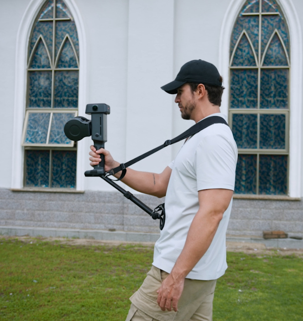 Operator walking a building exterior with a handheld XGRIDS scanner for mobile spatial capture of a facility.