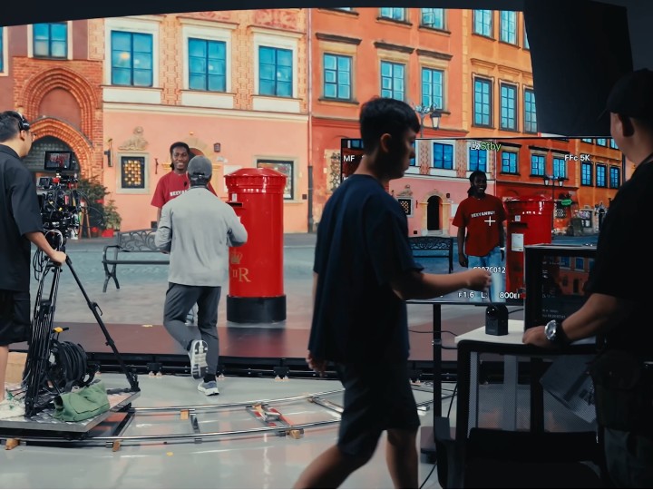 Film crew on an LED volume stage with a photoreal town-square environment on the wall, shooting a scene in virtual production.
