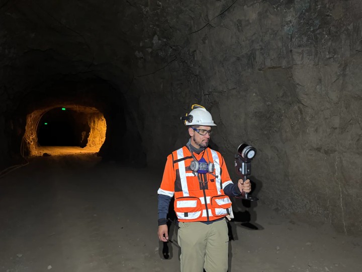 Surveyor in hi-vis gear holding a handheld Lixel scanner inside an underground mine tunnel, surveying the mining environment.