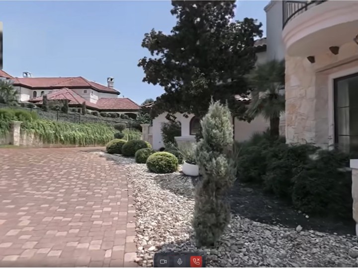 Photoreal 3D exterior of a Mediterranean-style estate with on-screen video-call controls for guided remote property viewing.