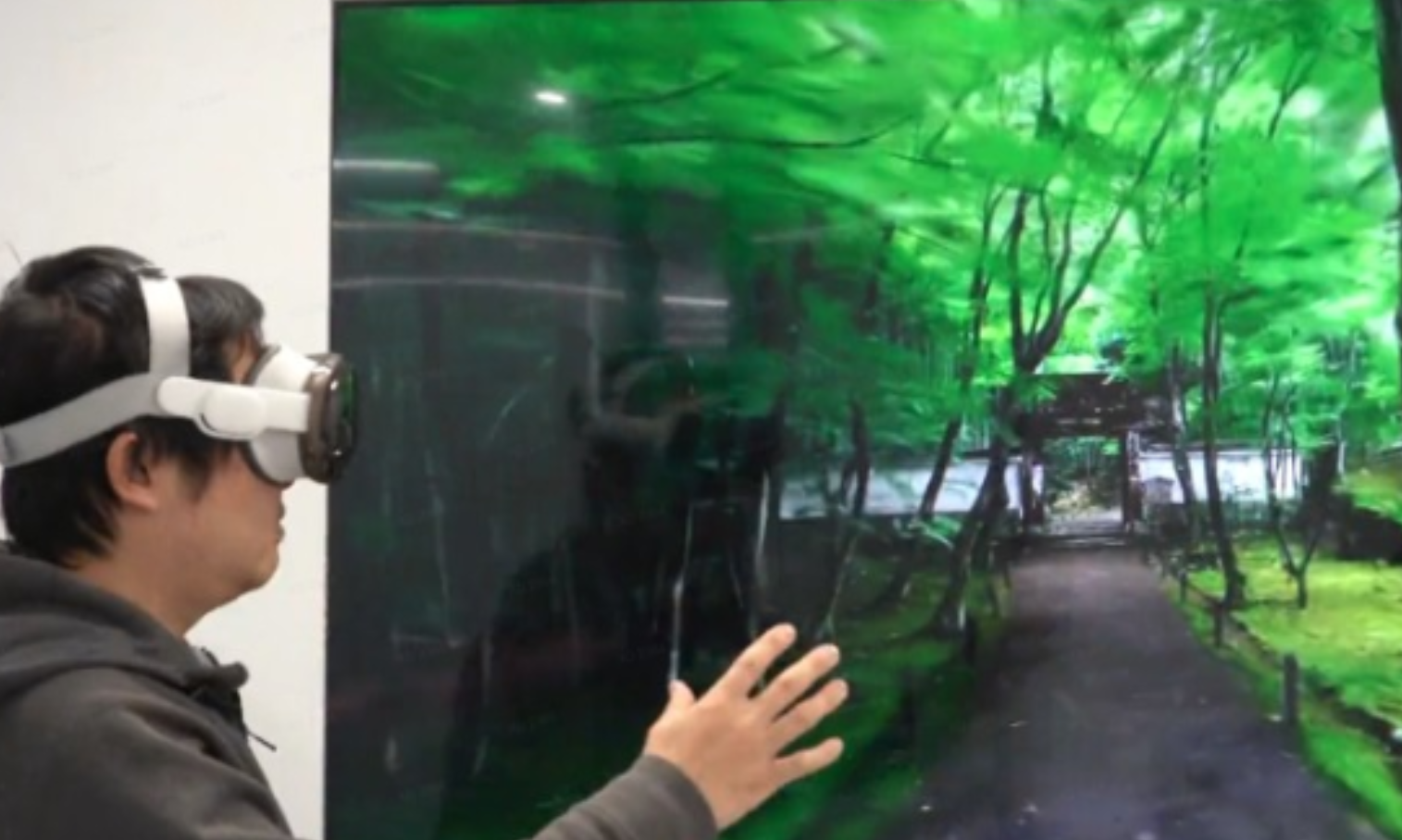 Person in a VR headset reaching toward a photoreal forest scene on screen, experiencing a 3DGS environment published to XR.